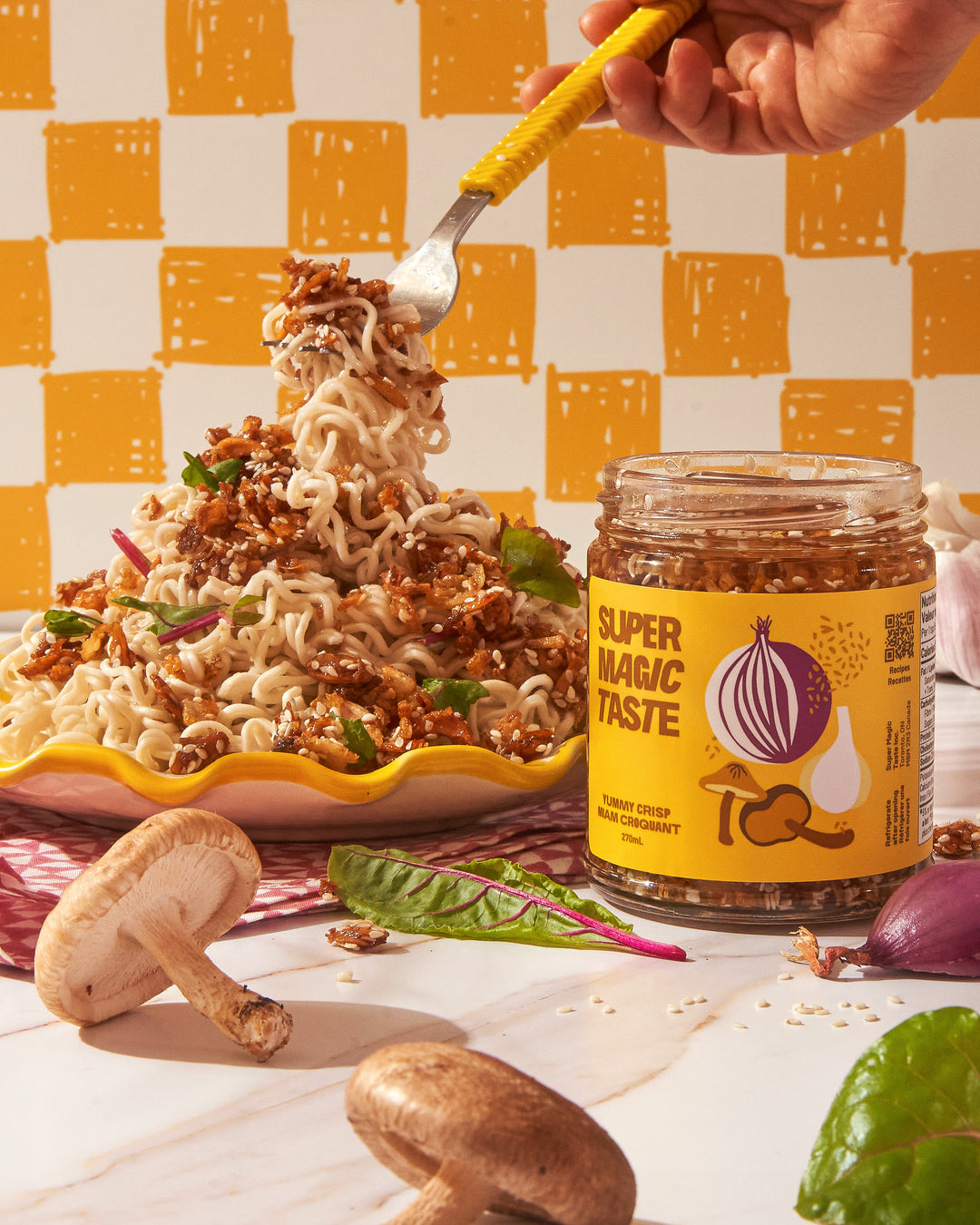A forkful of noodles lifted from a yellow bowl topped with Super Magic Taste Yummy Crisp, jar and shiitake mushrooms alongside.